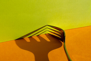 Close-up studio shot of the shadow of the tines of a fork on an orange and lime green background.