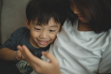 Little girls and boy siblings look at the phone and smile. They hold a smartphone watch videos,...