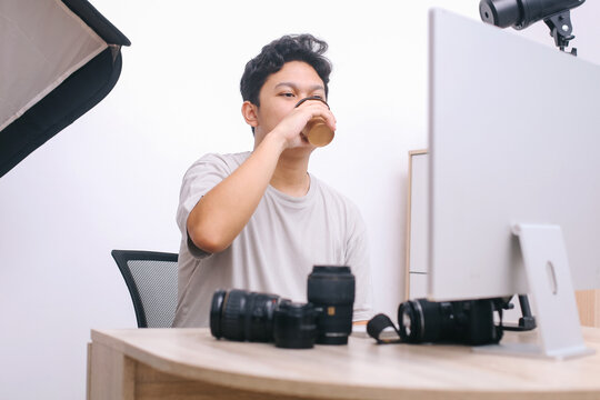 Young photo editor enjoying coffee while editing photo or video in front of the screen computer at production office