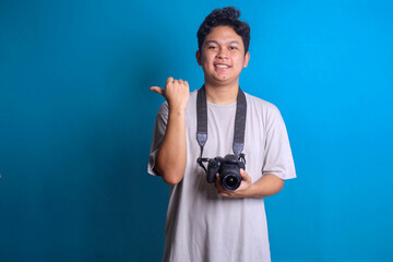 Portrait of young professional photographer smiling and holds camera while pointing finger to the side