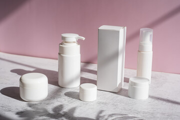 The white skincare set with pump, jar, and box and container on pink background.
