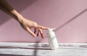 beauty hand is touching skincare pump on pink background for cosmetic and self care concept.
