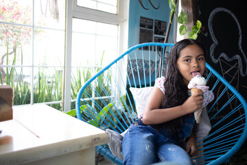 cute hipanic kid girl eating ice cream, cheerful latin child smiling holding a gelato at an...
