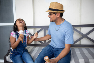 hispanic dad and daughter laughing together having an ice cream outdoors on summer