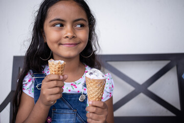 cute hispanic kid girl eating ice cream, cheerful latin child smiling holding a gelato at an...
