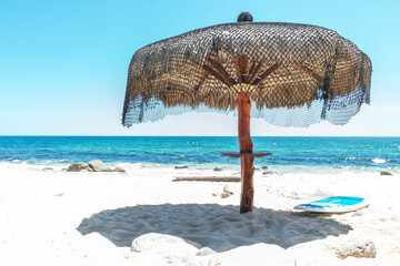 Thatch umbrella with surfboard on sunny beach in Mexico with ocean and sky background