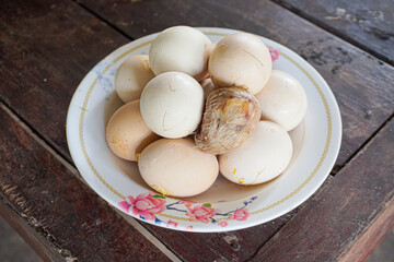 Pile of Steamed egg spoiled while being incubated on white plate place on wooden table. Eggs that do not hatch are hard-boiled. weird food.