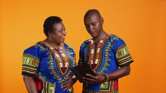 Ethnic people navigating on social media webpage, checking messages and looking at photos over orange background. African american man and woman scrolling online websites in studio.