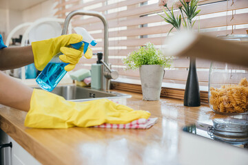 Maid in uniform working with spray bottle cleaning kitchen worktop. Emphasizing hygiene and safety...