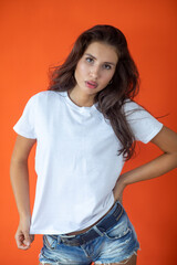Beautiful brunette girl in a white T-shirt and denim shorts posing on an orange background