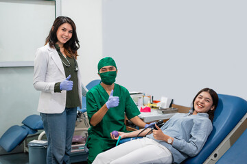 woman donor and two doctors smile at the camera with thumbs up in the blood transfusion room
