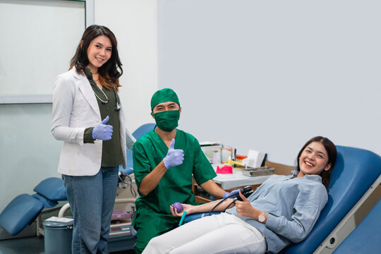woman donor and two doctors smile at the camera with thumbs up in the blood transfusion room - Powered by Adobe