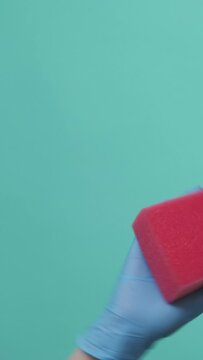 Vertical video. Household equipment. Surface wiping. Professional janitor hand in latex gloves cleaning washing with red sponge isolated on green background.