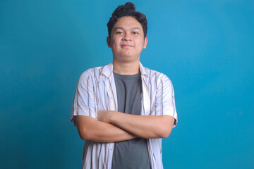 Portrait of confident young Asian male crossing arm over blue background