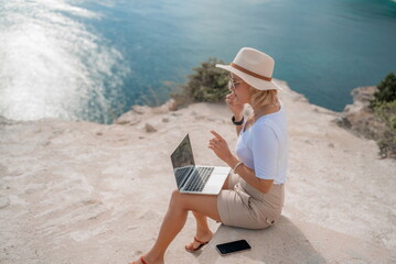 Freelance women sea working on the computer. Good looking middle aged woman typing on a laptop keyboard outdoors with a beautiful sea view. The concept of remote work.