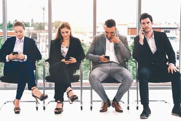 Businesswomen and businessmen using mobile phone while waiting on chairs in office for job interview. Corporate business and human resources concept. uds