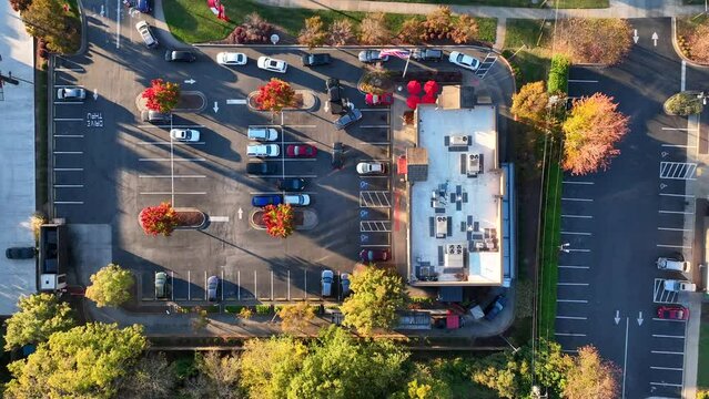 Heavy traffic at fast food restaurant drive through during autumn sunset. Top down aerial rising shot. American flag.