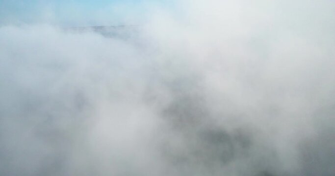 Aerial view through a thick, white fog cloud above the sea on a sunny morning