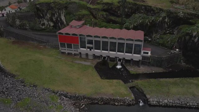 Aerial view of an hydroelectric power plant  on the river mouth, drone moving forward in direction of the power plant and camera tilting down. Porto Moniz Madeira island.