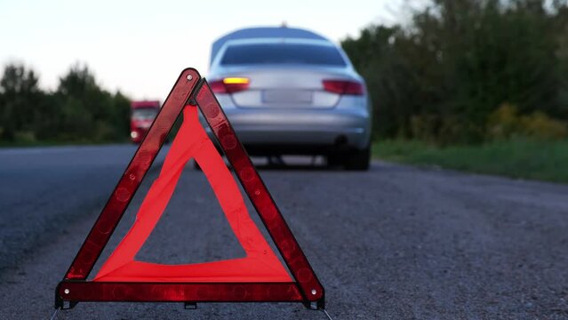 Broken silver luxury car emergency accident. Man driver installing red triangle stop sign on road. Sport automobile turned on blinkers technical problems on the road. Safety procedure when having