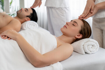 Caucasian couple enjoying relaxing anti-stress head massage and pampering facial beauty skin recreation leisure in dayspa modern light ambient at luxury resort or hotel spa salon. Quiescent - obrazy, fototapety, plakaty