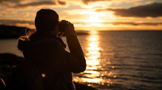  a woman taking a picture of a sunset over a body of water with the sun in the distance and clouds in the sky.