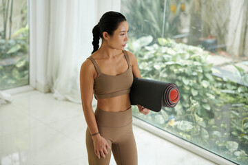 Portrait of fit young woman holding yoga mat and looking away