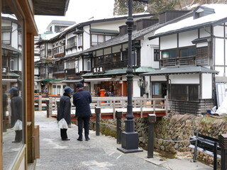 Obraz premium 雪の日の銀山温泉を歩く老夫婦 旅行 山形県 温泉街 温泉町 レトロ 歴史 観光 後ろ姿 シニア 温泉 川沿い