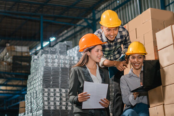 three Asian factory employees work on a laptop in the goods warehouse