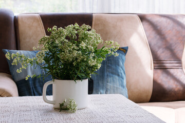 Interior. Room. Bouquet of white, field flowers in iron, rough. a white mug on a table covered with a lace tablecloth. Sofa, pillows from old jeans. Summer. Cosiness. Rustic. Country house.