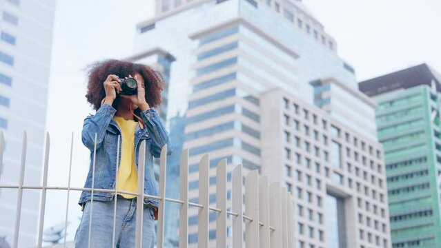 Attractive african teenager girl standing in the city, looking at around. Young tourist black woman happy and smiley, hair curly afro style, wearing jeans jacket and camera
