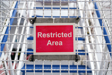 Fototapeta premium Close-Up Horizontal Frame of a Red Restricted Area Sign Attached to a White Netted Fence, No People, Daytime, Concept of Boundary and Security