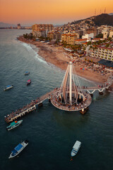 Closer view of Los Muertos Beach Pier at sunset with the sky illuminating at golden hour. Boats...