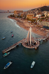 Closer view of Los Muertos Beach Pier at sunset with the sky illuminating at golden hour. Boats...