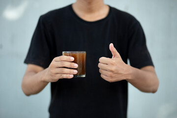 Front view close up of man hand holding coffee cup with thumbs up at home