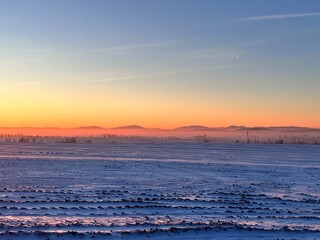 Winter landscape with snow-covered fields and mountains in the background at sunset