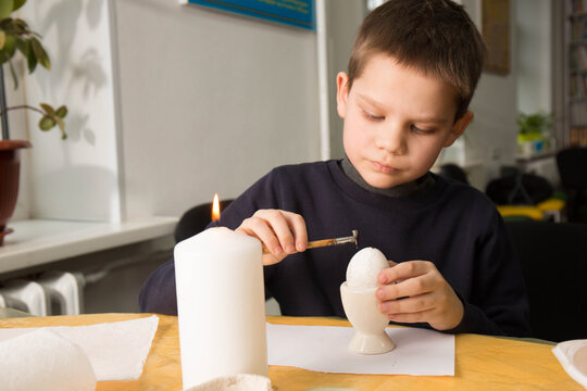 A boy makes a drawing with wax on an egg