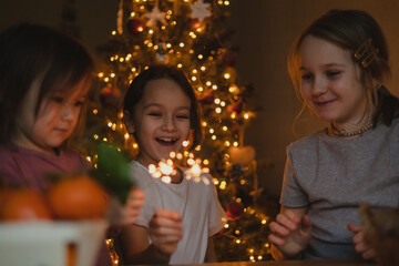 Obraz na płótnie Canvas three little girls celebrate Christmas at home, sparklers, tangerines.