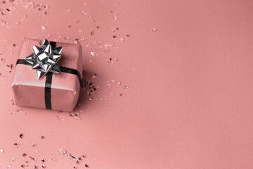 Pink gift with silver bow ribbon copy space with small shards of glass on a pink background 