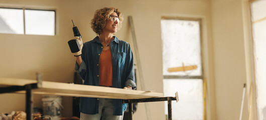 Happy home improvement: Skilled woman remodels kitchen with a drill gun for woodwork