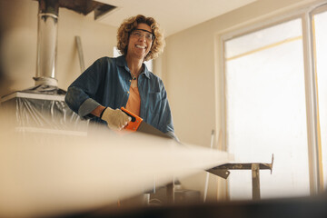 Happy mature woman in safety goggles working on a home renovation project with a crosscut saw