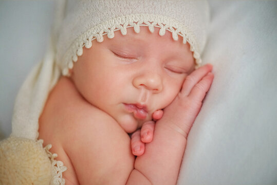 A newborn baby sleeps sweetly. Baby in a light cap. Younger brother. Portrait of a newborn. The baby lies with his cheek on his little hand. Boy in a hat. The baby is lying on his tummy. A happy famil