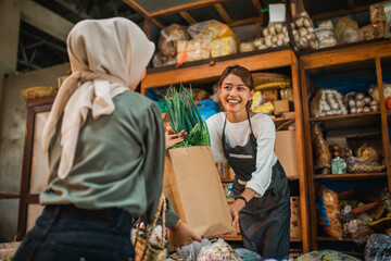 female green grocery seller giving her customer vegetables in paperbag
