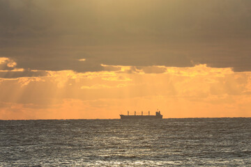 Obraz premium commercial cargo ship sailing in the sun and dark clouds