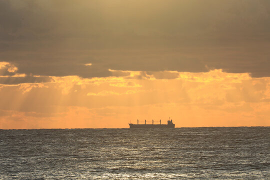 commercial cargo ship sailing in the sun and dark clouds