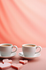 Obraz na płótnie Canvas Two cups of coffee on a pink background with heart-shaped candies