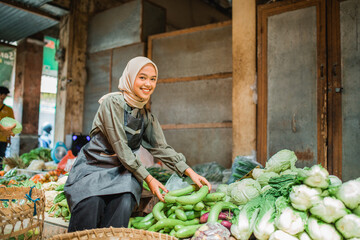 asian hijab vegetable seller looking at camera while arranging greengroceries at her stall