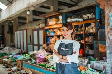 Deurstickers asian female vegetable seller standing in front of vegetables stall smiling with crossed arm © Odua Images
