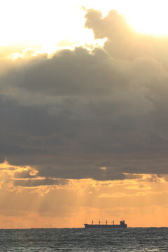 commercial cargo ship sailing in the sun and dark clouds