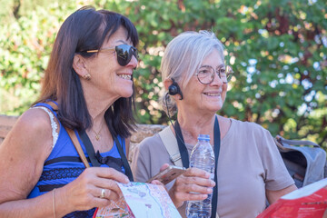 Joyful couple of senior females visiting European city listening to information via audio guide. Elderly couple of active women enjoying vacation and free time together